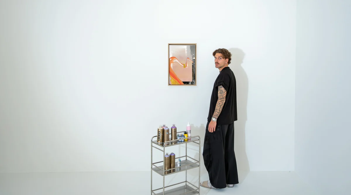 Valentin Nieroba stands next to a framed WAVES OF LIFE painting on the wall, spray cart in the foreground